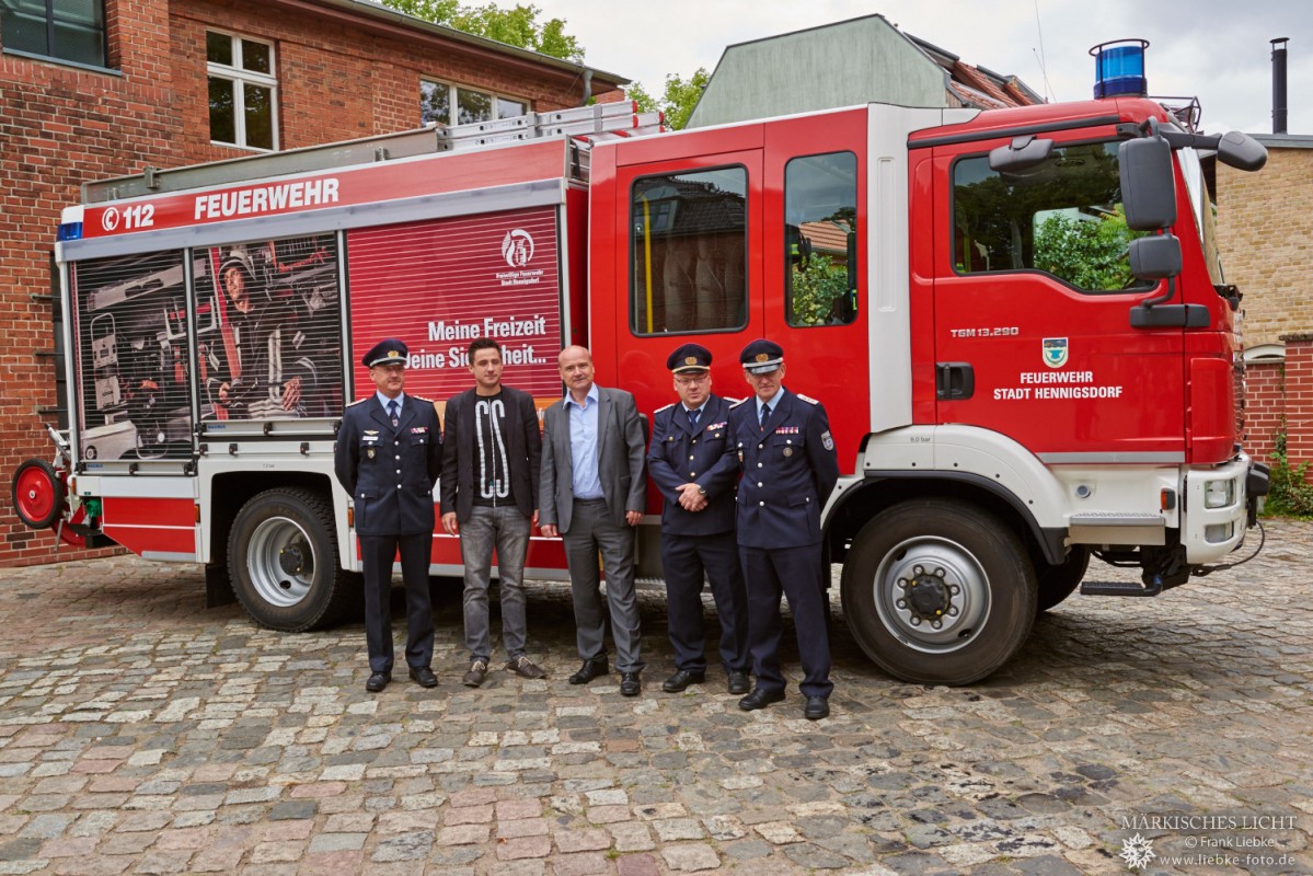 Gruppenbild vor dem gestalteten Löschfahrzeug der Hennigsdorfer Feuerwehr. Kameraden mit Bürgermeister (mitte) und Marketingbeauftragten (2.v.l.)